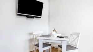 Ein weißer Esstisch mit zwei Stühlen, ein an der Wand befestigter Flachbildfernseher und ein kleiner Tisch mit einer Flasche und einer Fernbedienung.