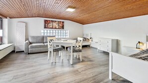 A modern bedroom with a wooden ceiling, a gray sofa, a white desk, and a bed with a patterned headboard. - Apartment 'Small Holiday  3 Monteurs' with Shared Garden and Wi-Fi (Weddingstedt)