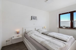 Une chambre à coucher avec un lit, des lampes de chevet, un tableau au mur et une fenêtre avec des stores.