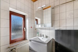 Een badkamer met een raam, wastafel, spiegel en radiator.