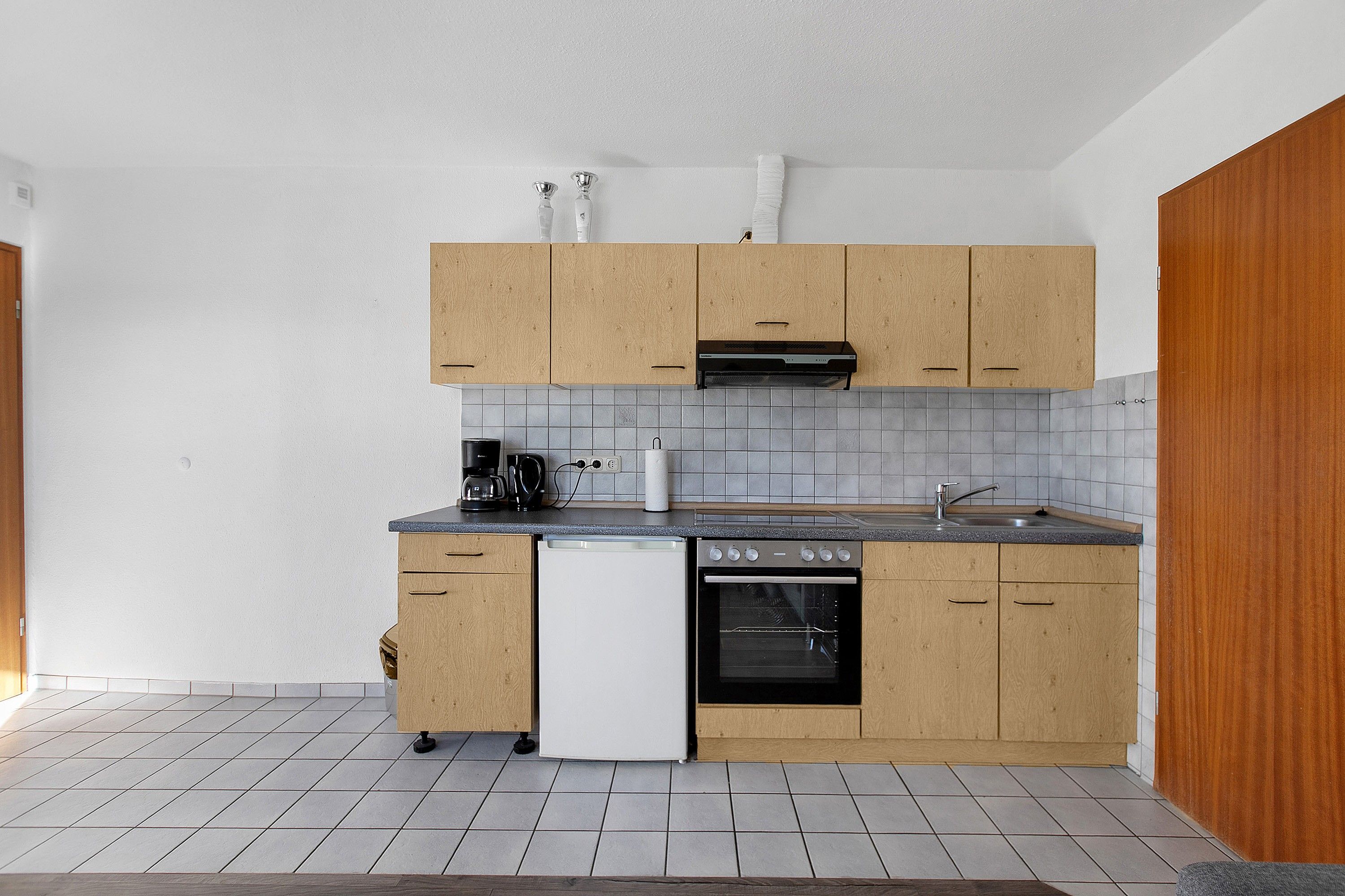 Une cuisine compacte avec des meubles de rangement en bois, un lave-vaisselle, une cuisinière et une machine à café.