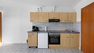 Une cuisine compacte avec des meubles de rangement en bois, un lave-vaisselle, une cuisinière et une machine à café.
