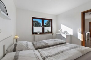 Een slaapkamer met twee bedden, een radiator, een raam met zonwering, een nachtkastje en een lamp.