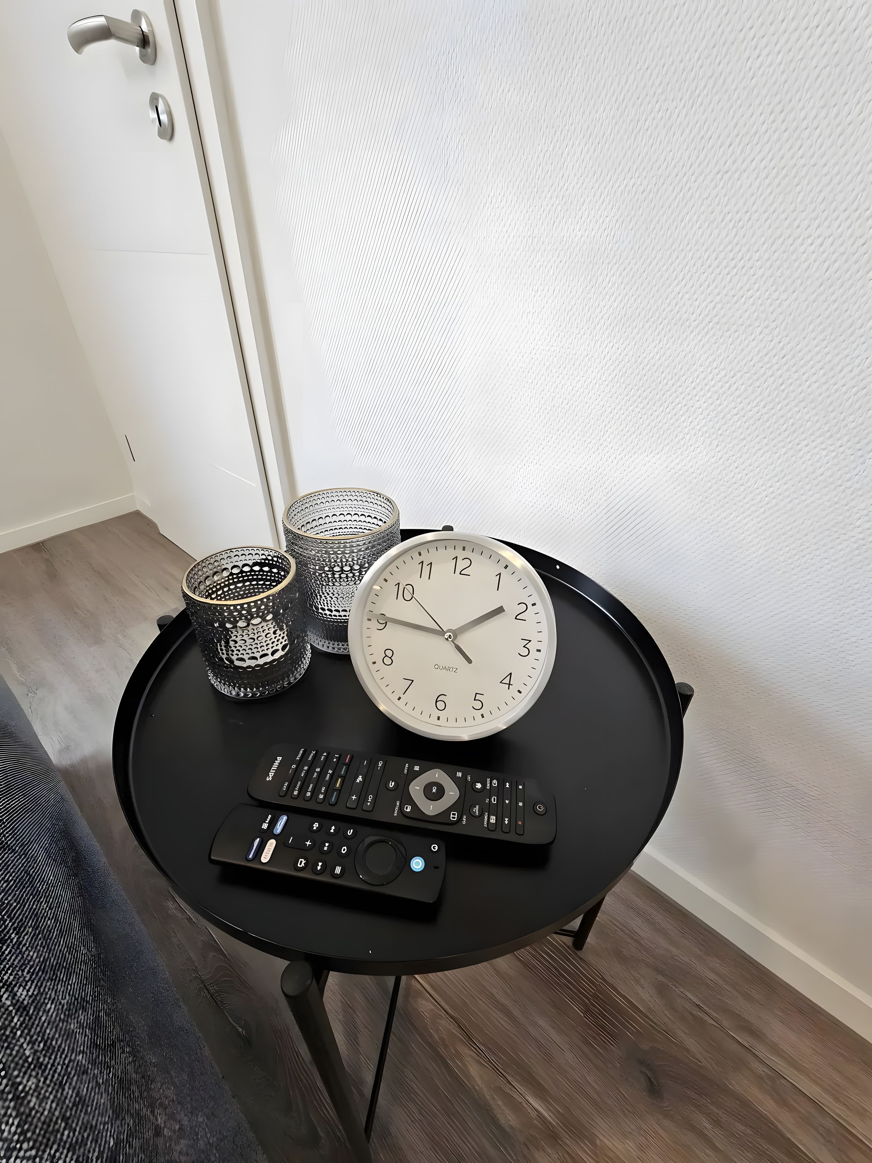 Een klein rond tafeltje met een klok, twee bekers met dessins en een afstandsbediening.
