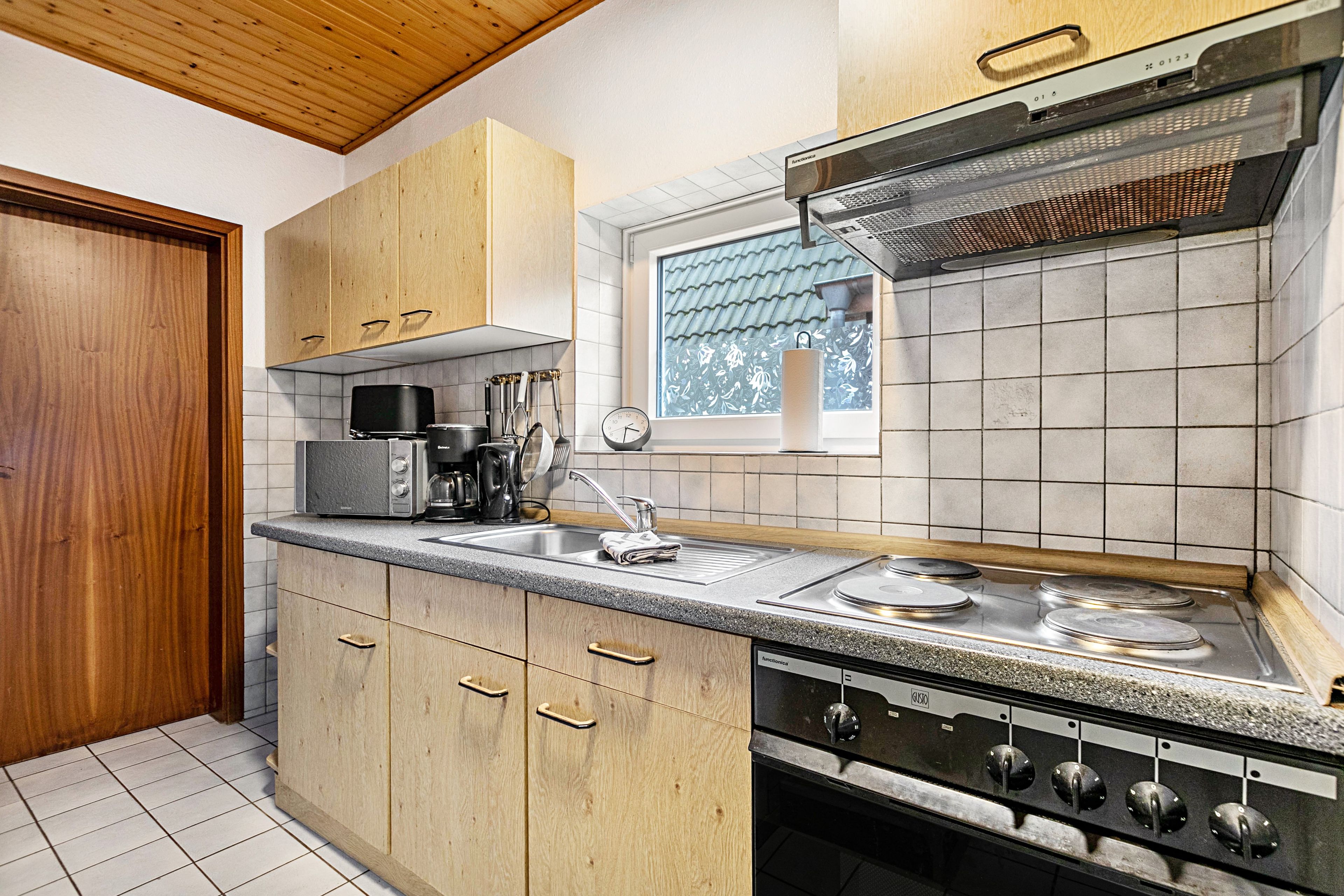 Une cuisine avec des meubles en bois, un four encastré et une fenêtre donnant sur l’extérieur.