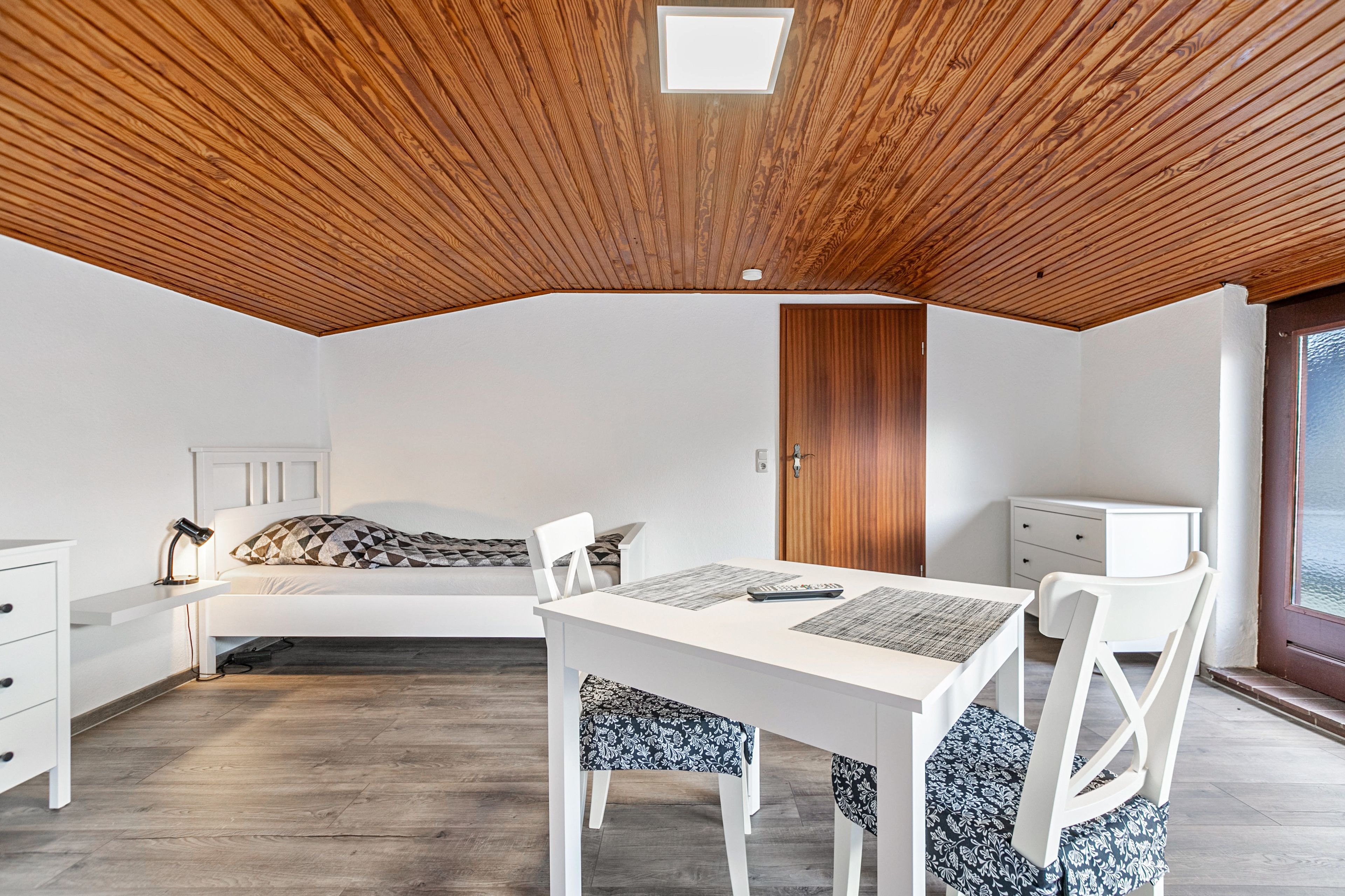 A room with a sloped ceiling, a bed, a desk, and a chair.