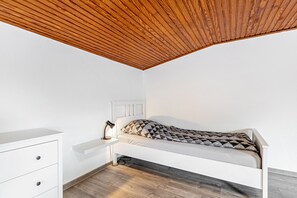 A bedroom with a sloped ceiling, a bed with a geometric-patterned pillow, a bedside table with a lamp, and a white dresser with drawers.
