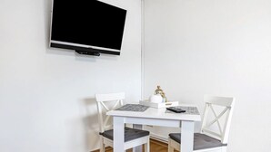 A white dining table with two chairs, a television mounted on the wall, and a bottle on the table. - Apartment "Practical Mechanic Room 5" with Shared Garden and Wi-Fi (Weddingstedt)