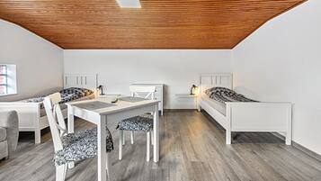 Een kamer met houten plafond, twee enkele bedden, een bureau met stoel, en een kleine tafel met lamp.