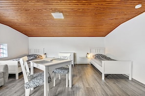 Een kamer met houten plafond, twee enkele bedden, een bureau met stoel, en een kleine tafel met lamp.