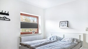 A bedroom with a bed, a window with blinds, a radiator, a picture on the wall, and a coat rack. - Apartment "Practical Mechanic Room 5" with Shared Garden and Wi-Fi (Weddingstedt)