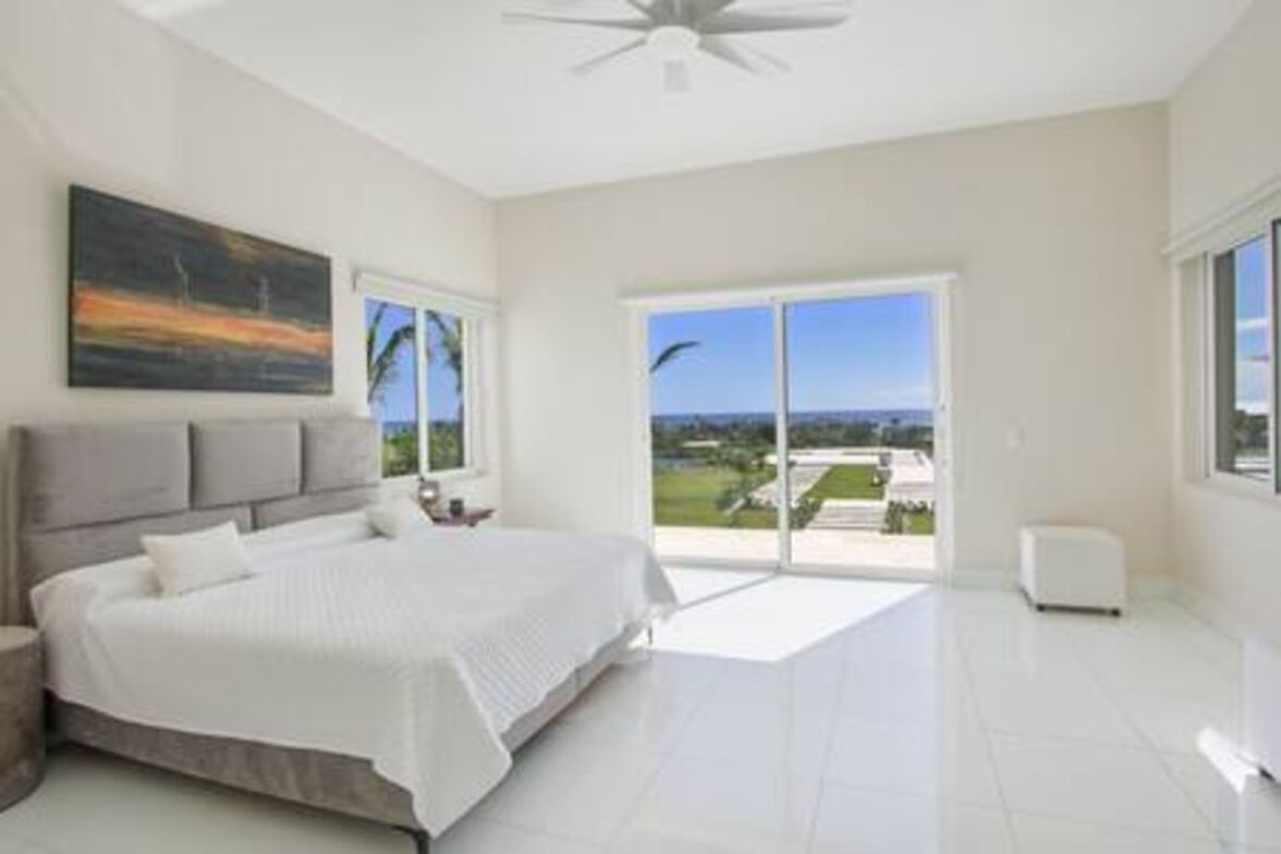Un dormitorio con una cama grande, un ventilador de techo y vistas al exterior a través de un ventanal corredero.