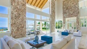 A spacious living room with a large window, a white sofa, and a coffee table. - Insane Ocean View Cap Cana Villa - Pool Chef Staff (Punta Cana)