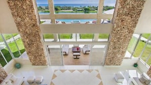 A spacious indoor area with a large window offering a view of a pool and greenery. - Insane Ocean View Cap Cana Villa - Pool Chef Staff (Punta Cana)