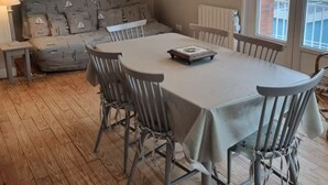 A dining area with a table, chairs, and a hanging light fixture. - The lighthouse facing the sea (Saint-Valery-en-Caux)