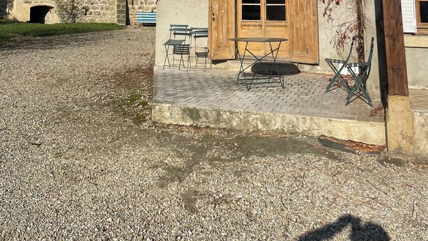 Un edificio rústico con pared de piedra, contraventanas de madera y un patio de grava.