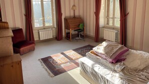 Una habitación con cama, escritorio, silla, radiador y ventanas con cortinas.