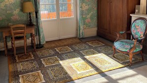 Una habitación con un armario de madera, un sillón estampado con motivos florales, una lámpara de pie y una alfombra con diseño.