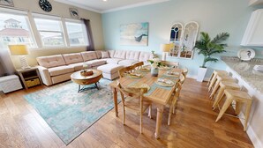 Un salon avec un canapé d’angle beige, une table basse ronde et un coin repas comprenant une table et des chaises en bois.