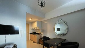 Um espaço compacto com mesa de jantar, duas cadeiras, televisão, espelho e cozinha compacta ao fundo.