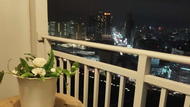 Uma varanda com uma planta em vaso e vista para a paisagem urbana à noite.