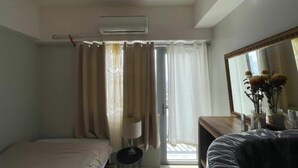 Quarto com cama, mesa de cabeceira com abajur, cômoda, espelho e janela com cortinas.