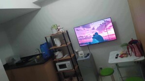 Uma cozinha compacta com televisão de tela plana na parede, micro-ondas e um refrigerador pequeno.