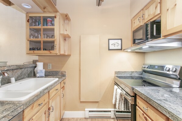 A compact kitchen with wooden cabinets, a granite countertop, a stainless steel stove, and a microwave. - Brooktree Condos D221 2 Bedroom Condo (Vail)