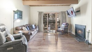 A living room with leather sofas, a glass coffee table, a fireplace, and a TV mounted on the wall. - Brooktree Condos D221 2 Bedroom Condo (Vail)