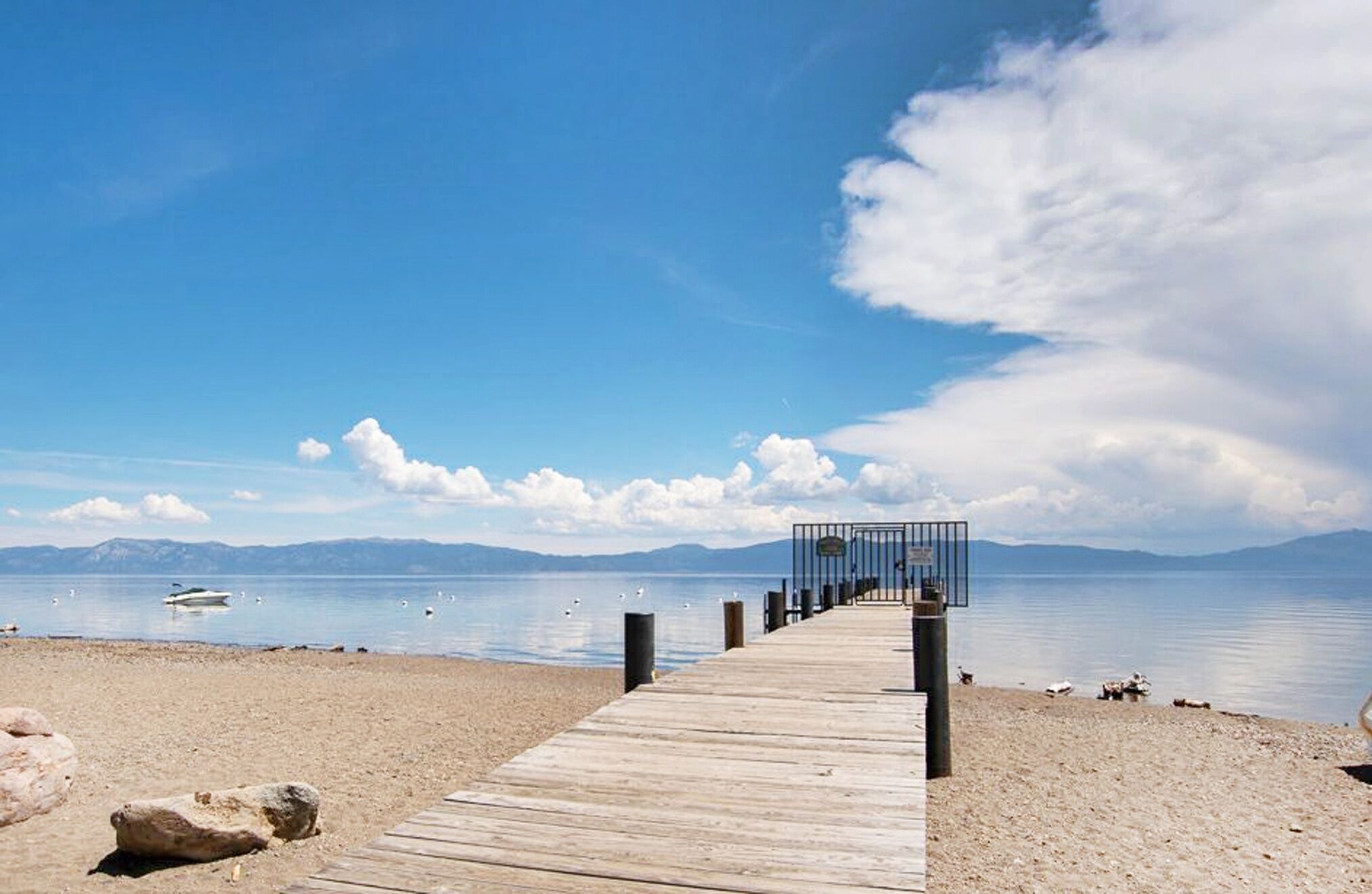 A wooden pier leading to a beach with a clear sky and mountains in the distance.