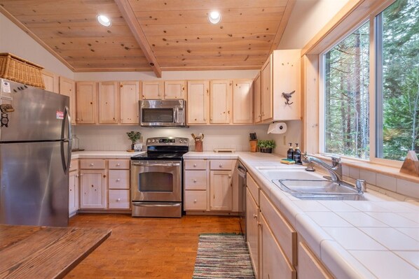 Une cuisine moderne avec des meubles en bois, des appareils électroménagers en acier inoxydable et une grande fenêtre donnant sur la forêt.