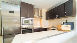 Una cocina moderna con electrodomésticos de acero inoxidable, armarios de madera oscura y una encimera blanca.