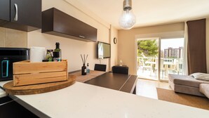 Una cocina moderna con armarios oscuros, una isla de madera y un comedor con mesa y sillas. Una ventana grande ofrece vistas al exterior.