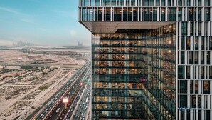 A high-rise building with multiple floors, large windows, and a view of a busy highway and distant cityscape. - WYZ RENT|2BR Vida Dubai Mall Direct Mall Access (Dubai)
