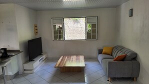 A living room with a grey sofa, a wooden coffee table, a TV on a stand, and a window with shutters. - Les terrasses de Maëlle II - Pretty villa with pool and sea view in Rivière-Salée (Rivière-Salée)