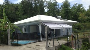 A covered outdoor area with a pool, a fenced patio, and a building with a white roof. - Les terrasses de Maëlle II - Pretty villa with pool and sea view in Rivière-Salée (Rivière-Salée)
