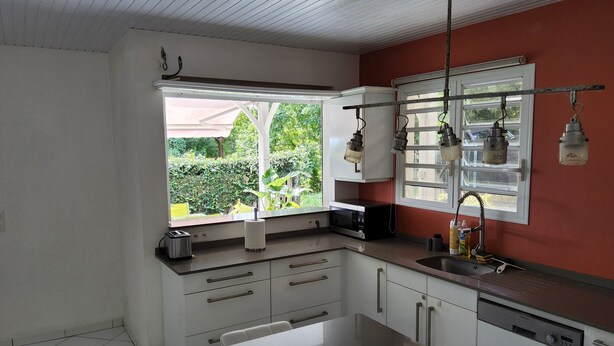 A kitchen with white cabinets, a black microwave, and a window with a view of greenery. - Les terrasses de Maëlle II - Pretty villa with pool and sea view in Rivière-Salée (Rivière-Salée)