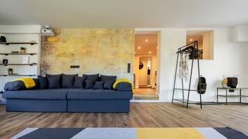 Ein modernes Wohnzimmer mit einem dunkelblauen Sofa, Holzdielen und einer strukturierten Wand.