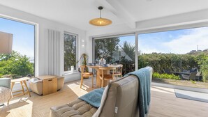 A modern living room with a large window, a round wooden table, and a beige sofa. - Beautiful 4-bedroom house with stunning sea views in the village of Guileen (Whitegate)