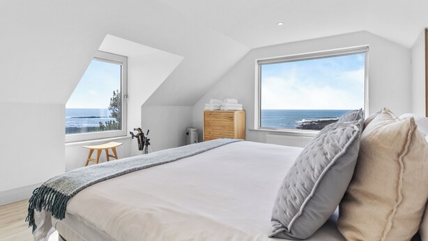 A bedroom with a large bed, a view of the sea, a wooden cabinet, and a small table. - Beautiful 4-bedroom house with stunning sea views in the village of Guileen (Whitegate)