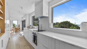 A modern kitchen with white cabinetry, a built-in oven, and a large window offering a view of greenery. - Beautiful 4-bedroom house with stunning sea views in the village of Guileen (Whitegate)