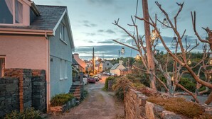 A narrow street with houses on both sides, a stone wall on the left, and bare branches on the right. - Beautiful 4-bedroom house with stunning sea views in the village of Guileen (Whitegate)