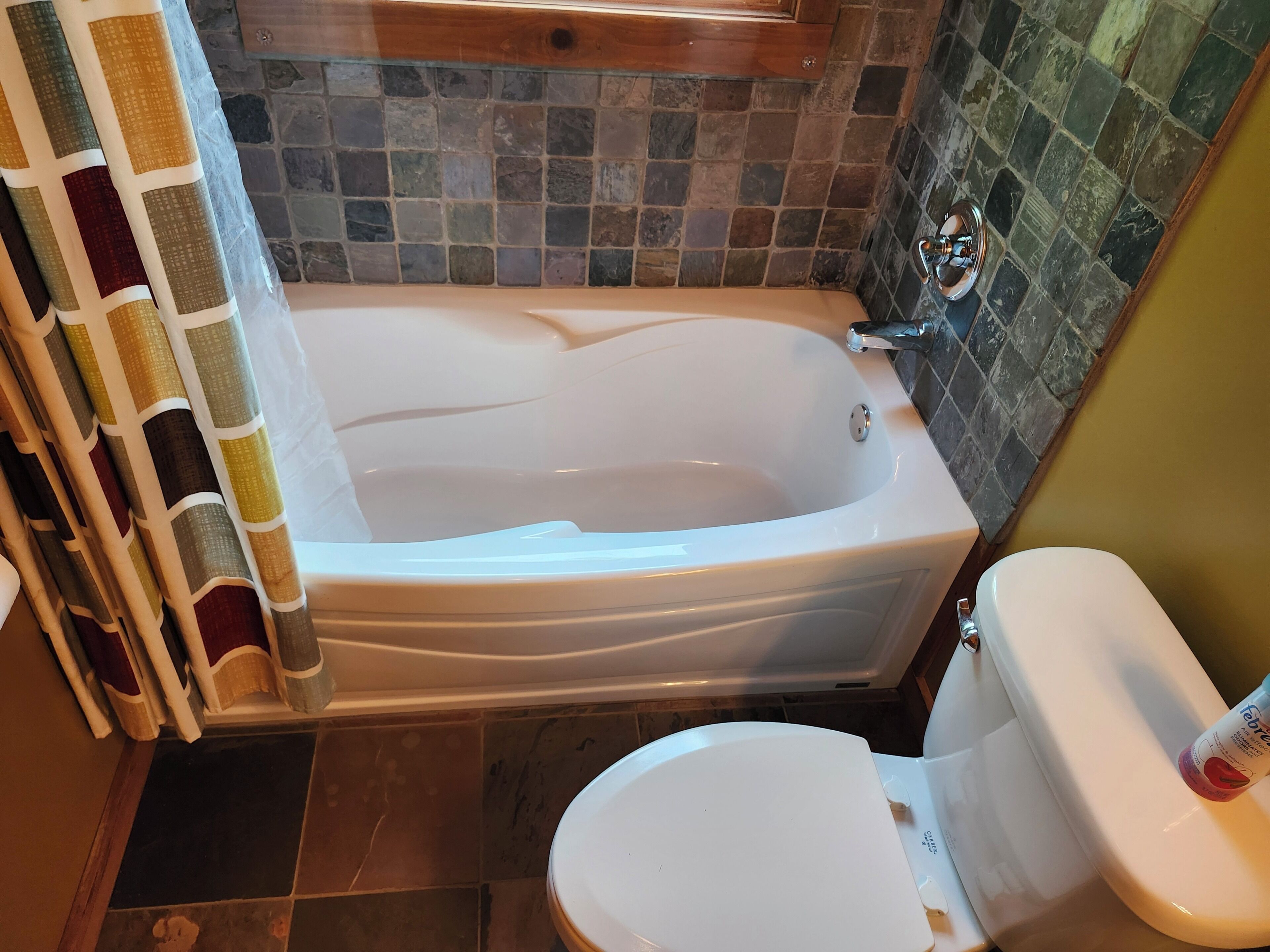 A bathroom with a bathtub, toilet, and tiled walls.