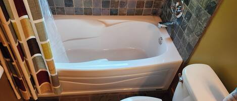A bathroom with a bathtub, toilet, and tiled walls.