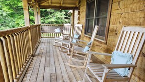 Une véranda en bois, avec des fauteuils à bascule et une table, donnant sur une zone boisée.