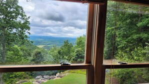Une vue à travers une fenêtre à cadre en bois, donnant sur un paysage verdoyant et luxuriant, avec des arbres et une vue lointaine sur des collines.