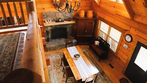 Un intérieur de chalet chaleureux avec une cheminée en pierre, une table à manger en bois et un lustre.