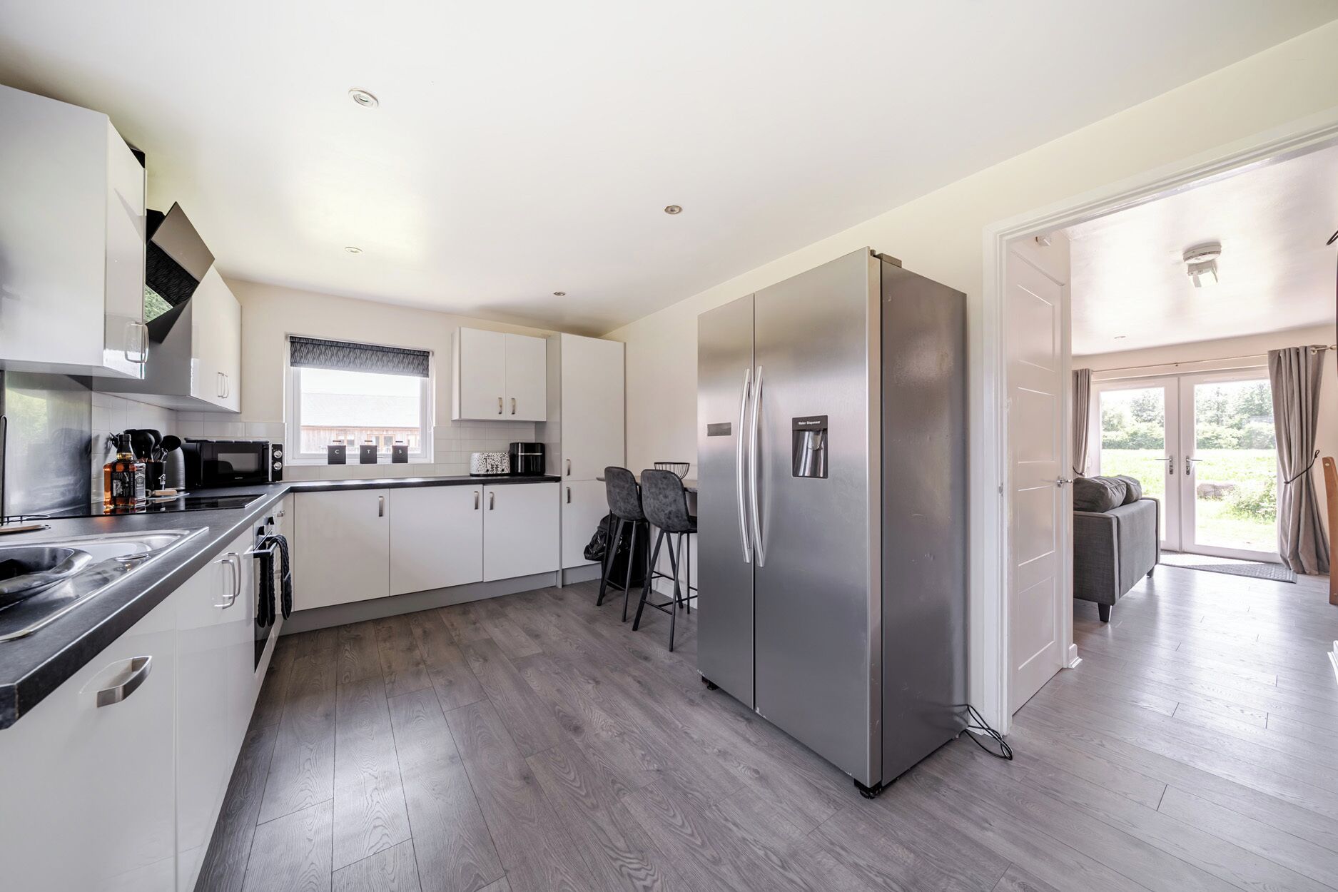A modern kitchen with white cabinets, a stainless steel refrigerator, and a dining area with two chairs.