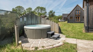 A hot tub in a backyard with a wooden fence, a stone pathway, and a wooden house in the background. - Raven Lodge (Brigg)