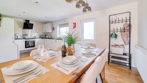 Una cucina moderna con mobili bianchi, una cappa aspirante nera e un'area pranzo con un tavolo di legno, piatti bianchi e bicchieri da vino.